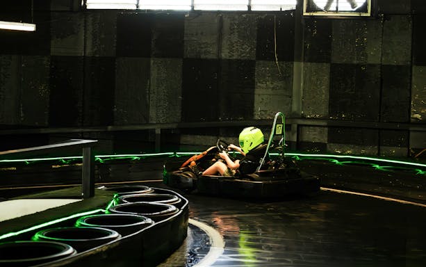 Indoor karting track with racer wearing a helmet navigating a curve.