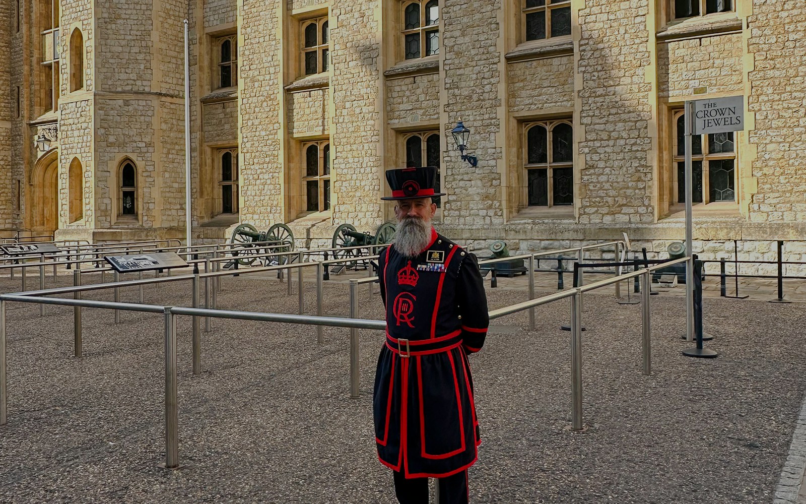 Beefeater in traditional uniform at the Tower of London near the Crown Jewels sign.