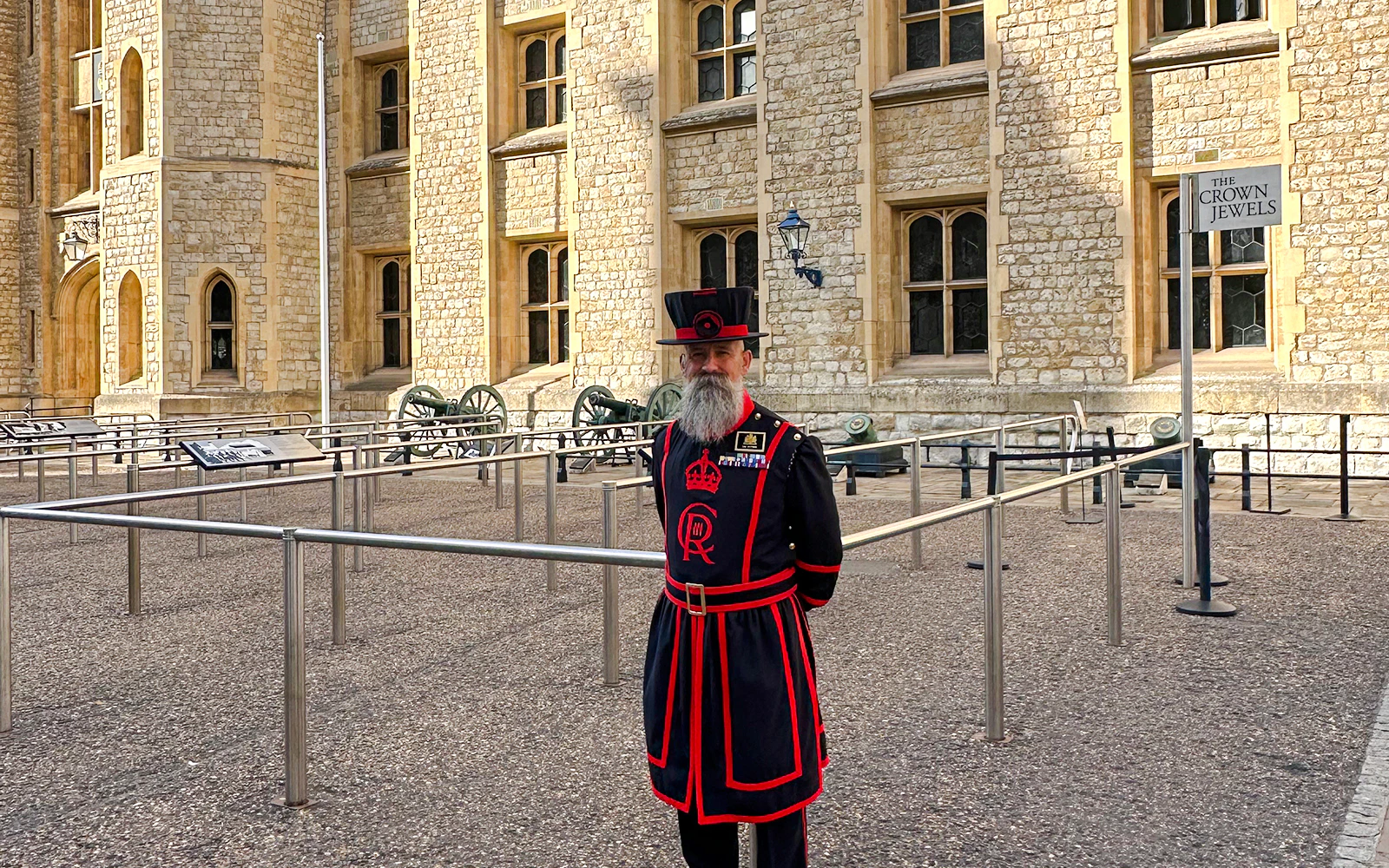 Beefeater in traditional uniform at the Tower of London near the Crown Jewels sign.