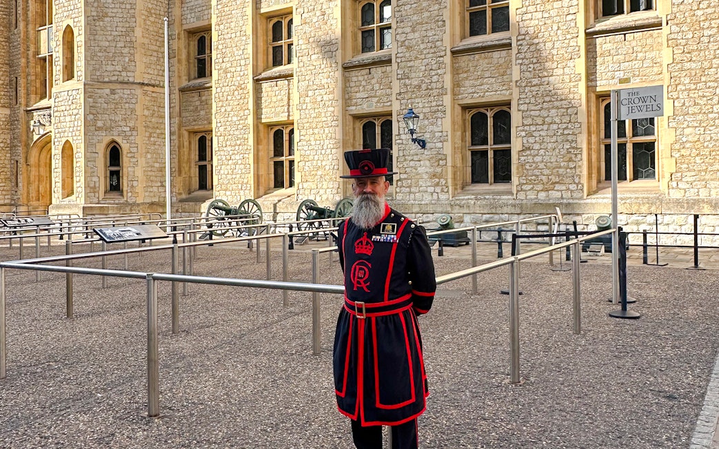 Beefeater in traditional uniform at the Tower of London near the Crown Jewels sign.