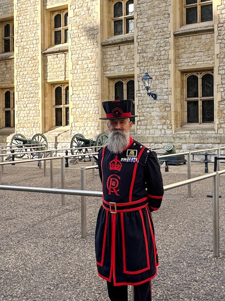 Beefeater in traditional uniform at the Tower of London near the Crown Jewels sign.