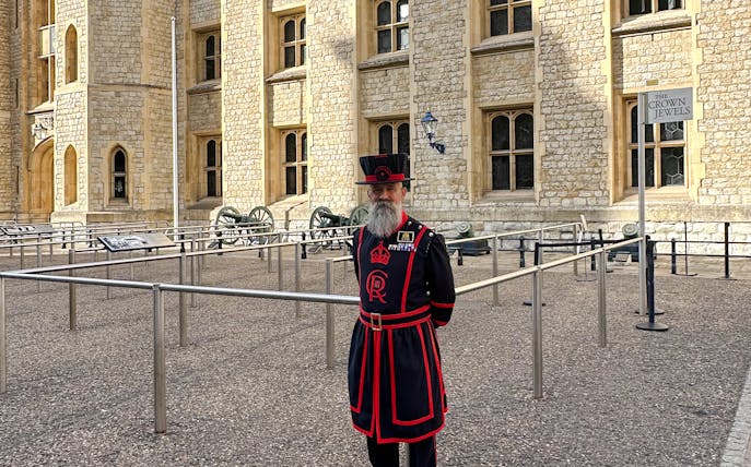 Beefeater in traditional uniform at the Tower of London near the Crown Jewels sign.
