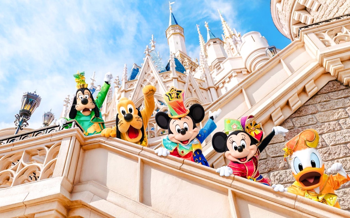 Mickey Mouse and friends in colorful outfits at Tokyo Disneyland castle.