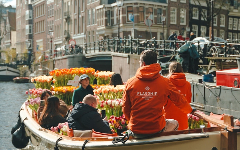Guests enjoying tulip cruise on Amsterdam canal with colorful flowers.