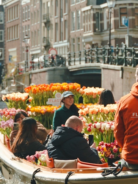 Guests enjoying tulip cruise on Amsterdam canal with colorful flowers.