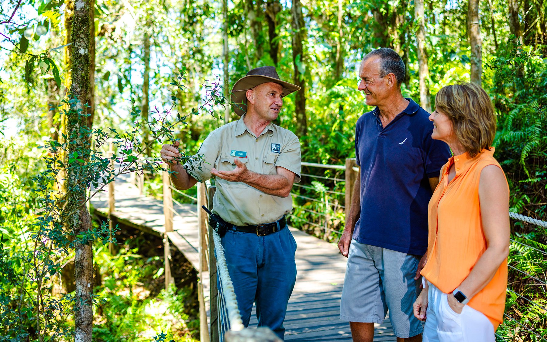 Guide explaining rainforest plants to tourists on Kuranda Scenic Train and Skyrail tour.