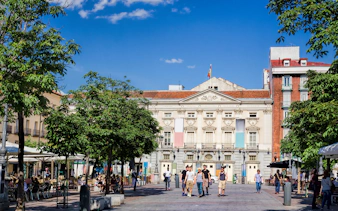 Plaza de Santa Ana in Madrid with people walking and cafes lining the square.