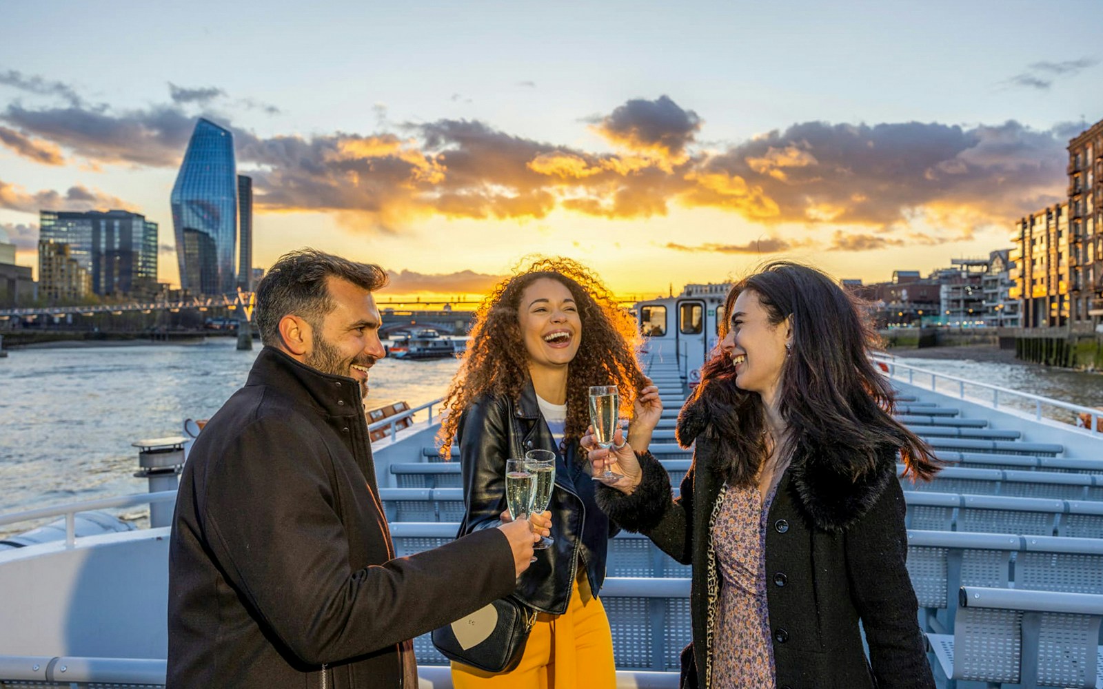 Passengers enjoying a Thames River Evening Cruise with sunset views, sipping sparkling wine and eating canapés on the deck