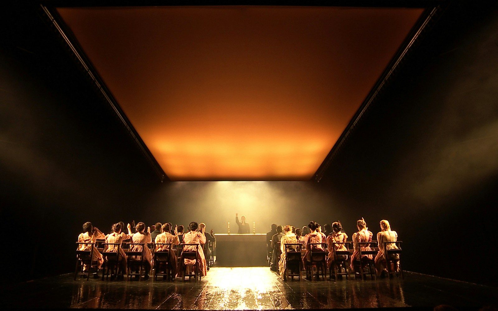 Theater performance of "The Crucible" with actors seated at a long table under dramatic lighting.