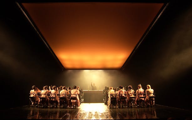Theater performance of "The Crucible" with actors seated at a long table under dramatic lighting.