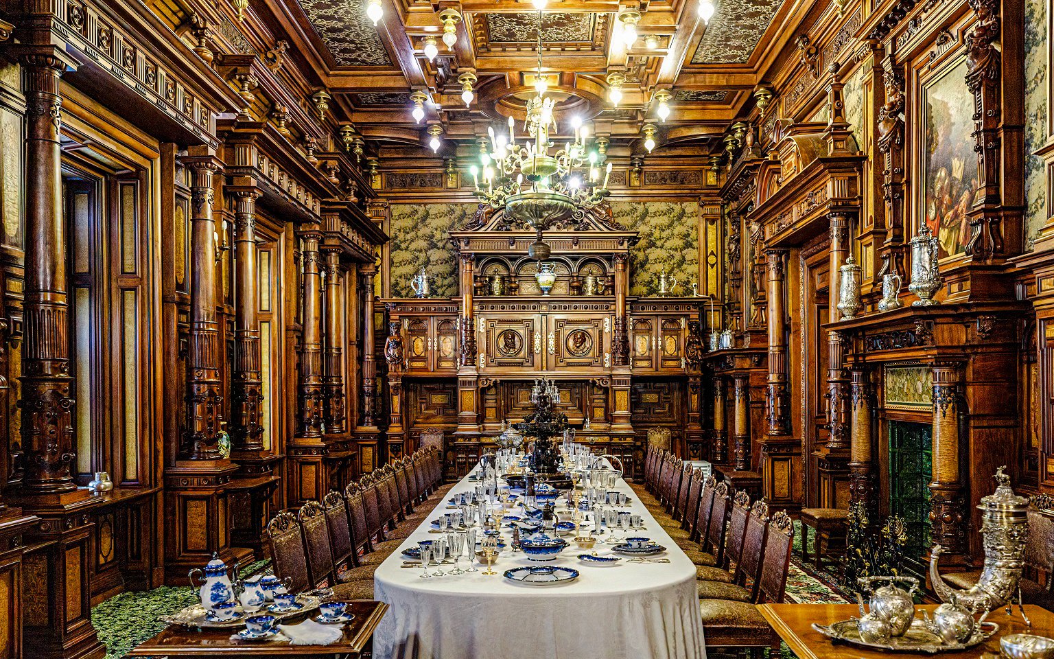 Peles Castle dining room with ornate woodwork and long table set for a banquet, Romania.