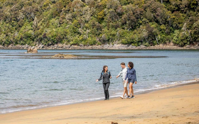 Visitors walking along the beach on Ulva Island with forested backdrop.