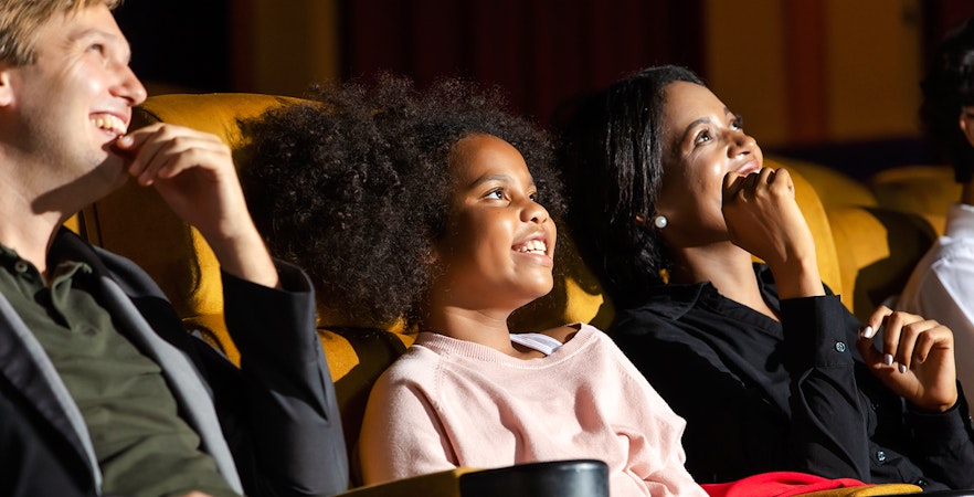 Family enjoying a movie in a theater, smiling and relaxed.