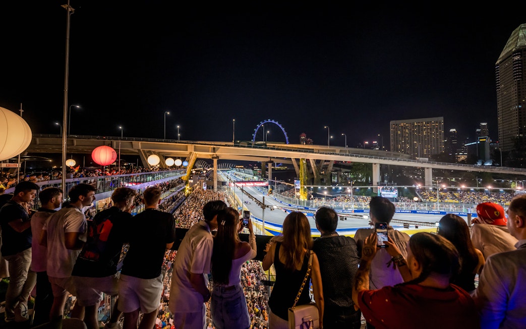 Crowd watching a night race with city skyline and Ferris wheel in the background.