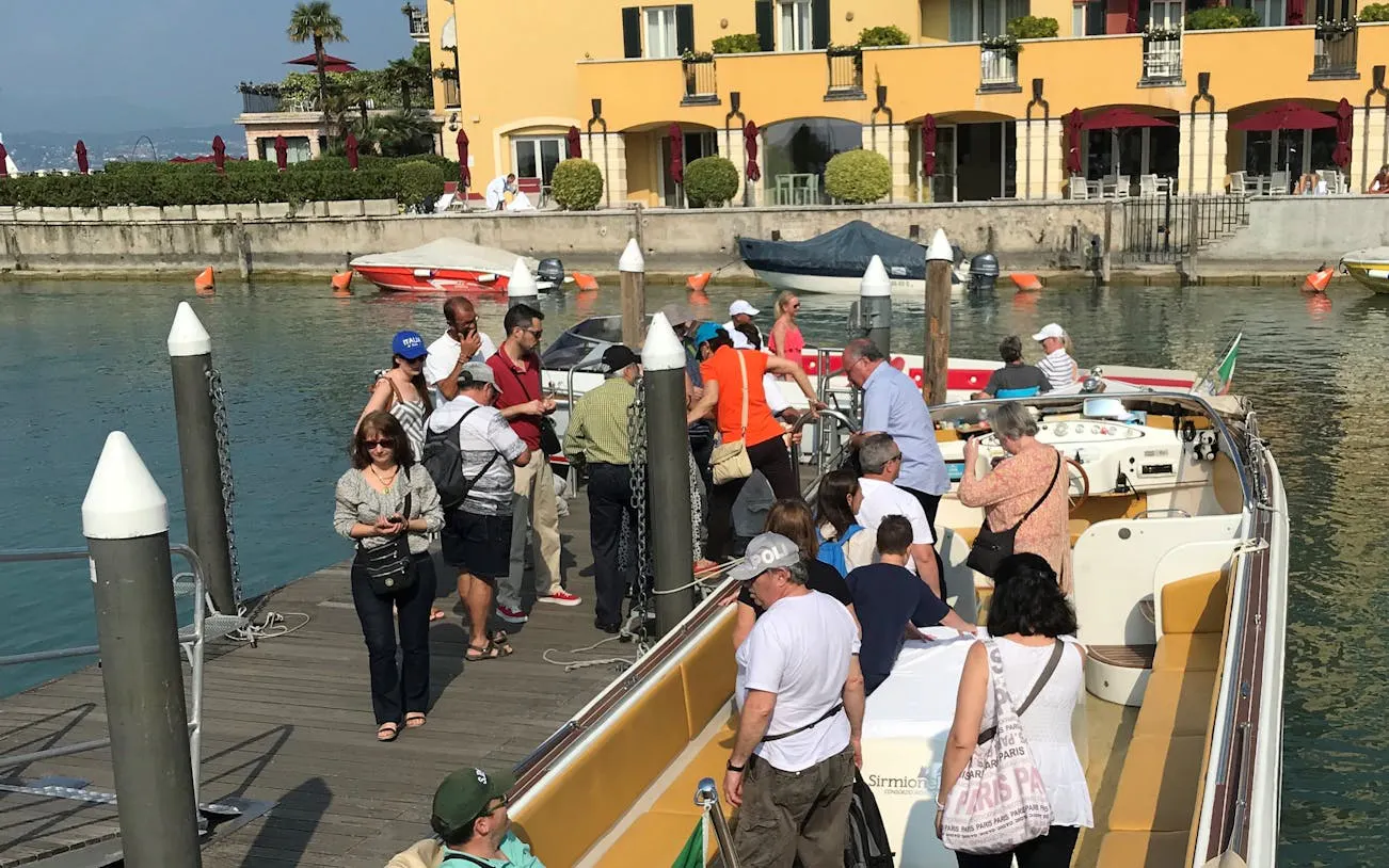 Tourists boarding a boat in Sirmione for a full-day tour to Lazise and Madonna della Corona Sanctuary.