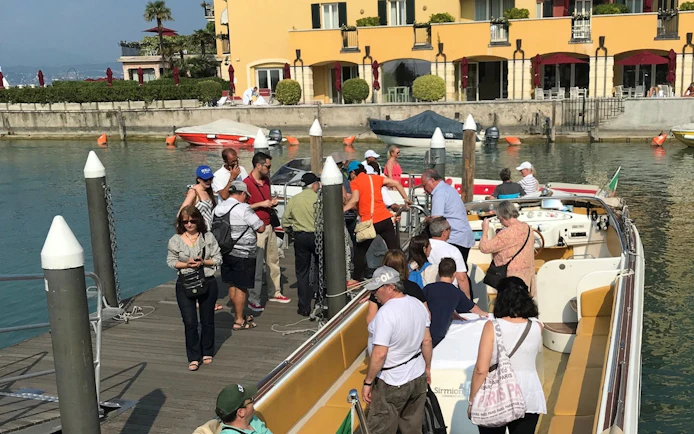 Tourists boarding a boat in Sirmione for a full-day tour to Lazise and Madonna della Corona Sanctuary.