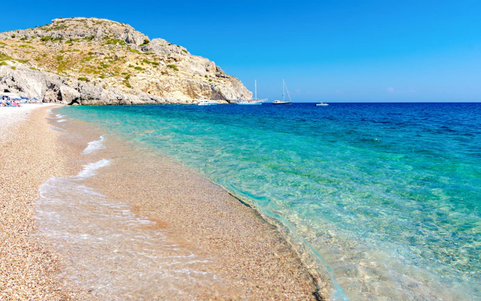 Afandou Beach shoreline with clear blue water and boats, Rhodes island, Greece.
