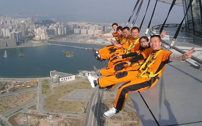 Group of friends sitting on Skypark Macau edge with city view.