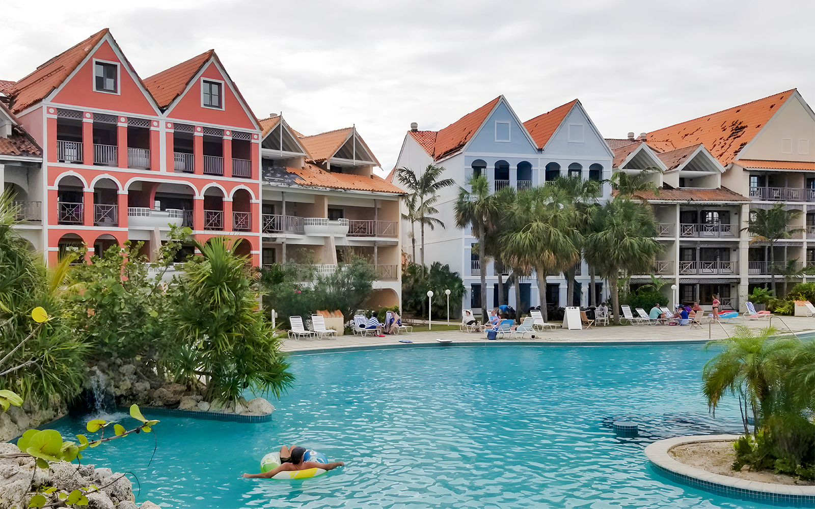 Taino Beach Resort pool area with colorful buildings and palm trees in the background.