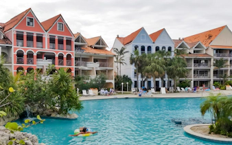Taino Beach Resort pool area with colorful buildings and palm trees in the background.