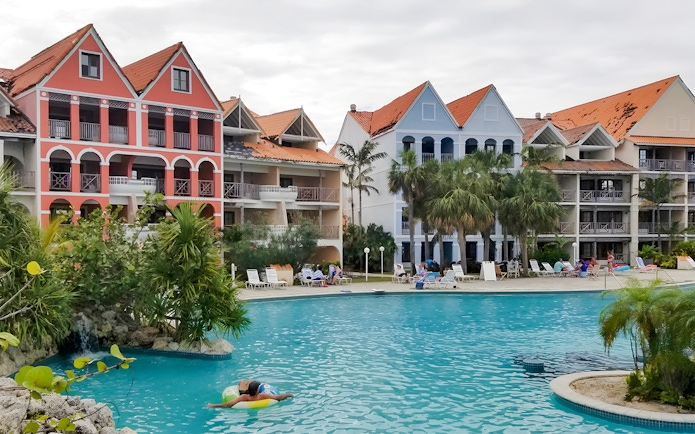 Taino Beach Resort pool area with colorful buildings and palm trees in the background.