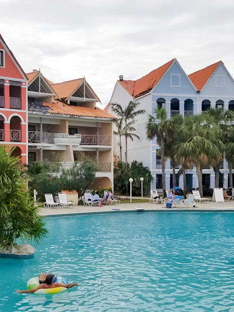 Taino Beach Resort pool area with colorful buildings and palm trees in the background.