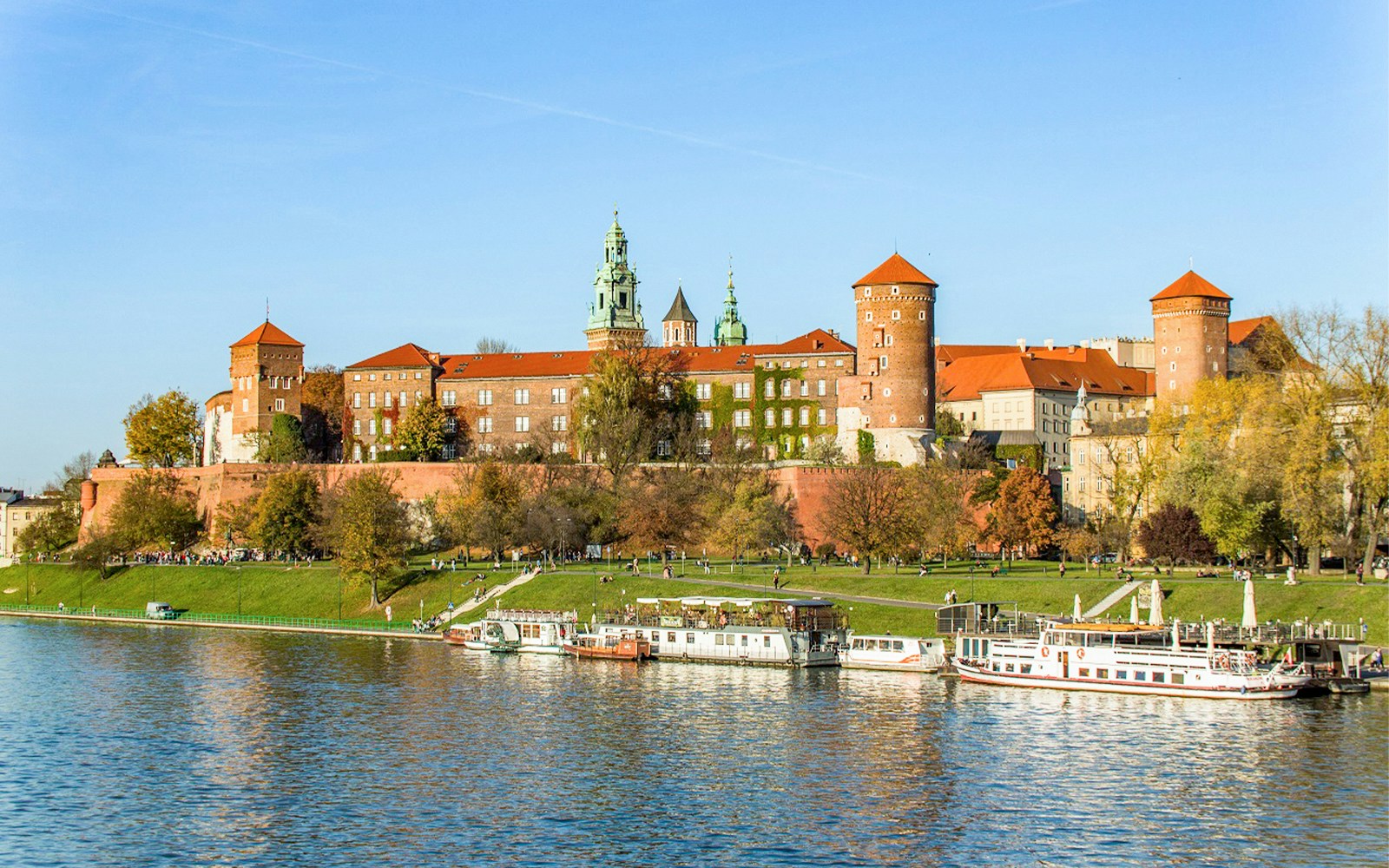 Catamaran cruising on Vistula River with Krakow's historic skyline in the background.