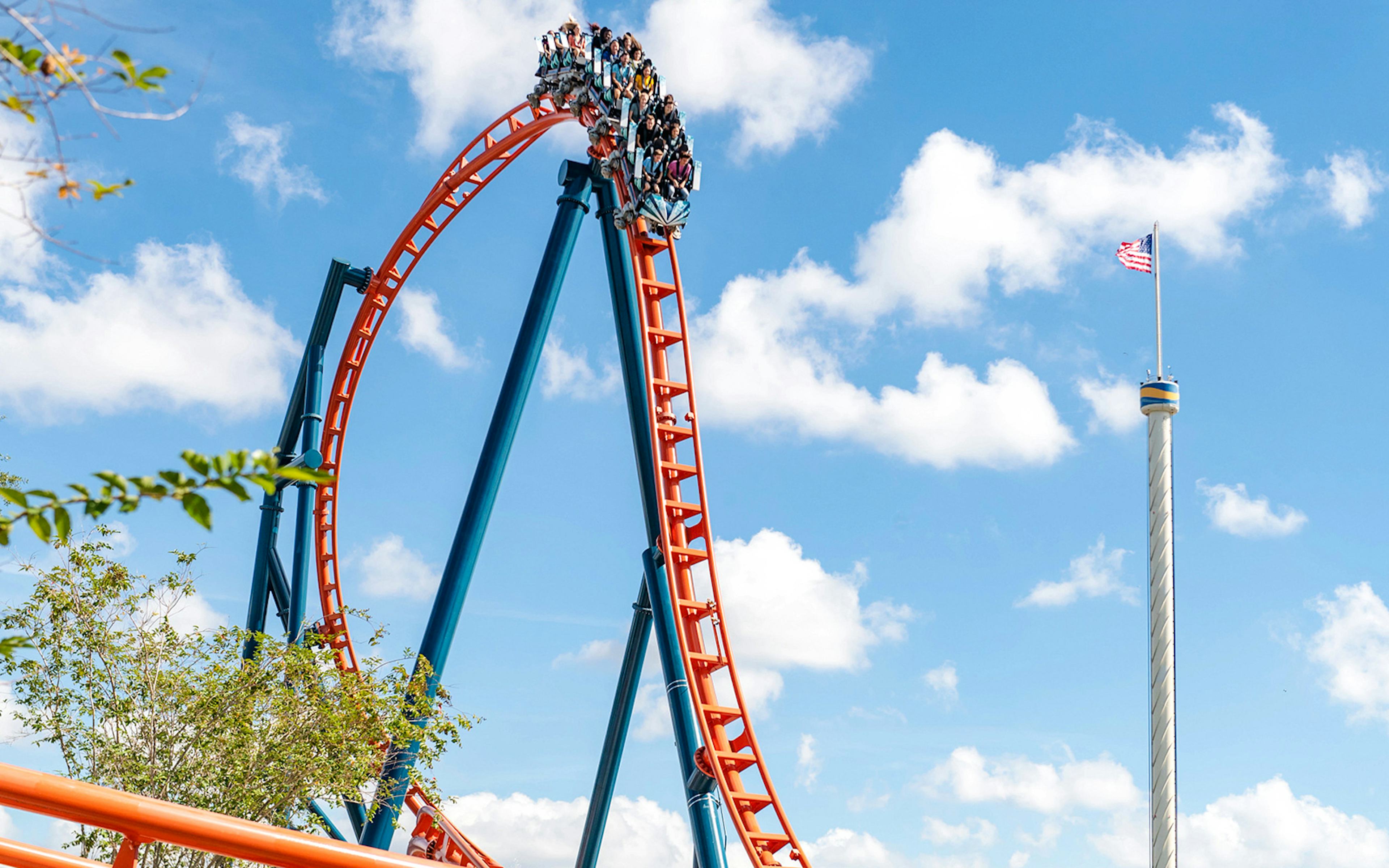 Roller coaster loop with riders on Ice Breaker at SeaWorld Orlando against blue sky.