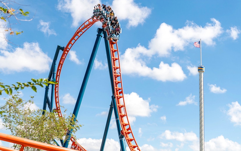 Roller coaster loop with riders on Ice Breaker at SeaWorld Orlando against blue sky.