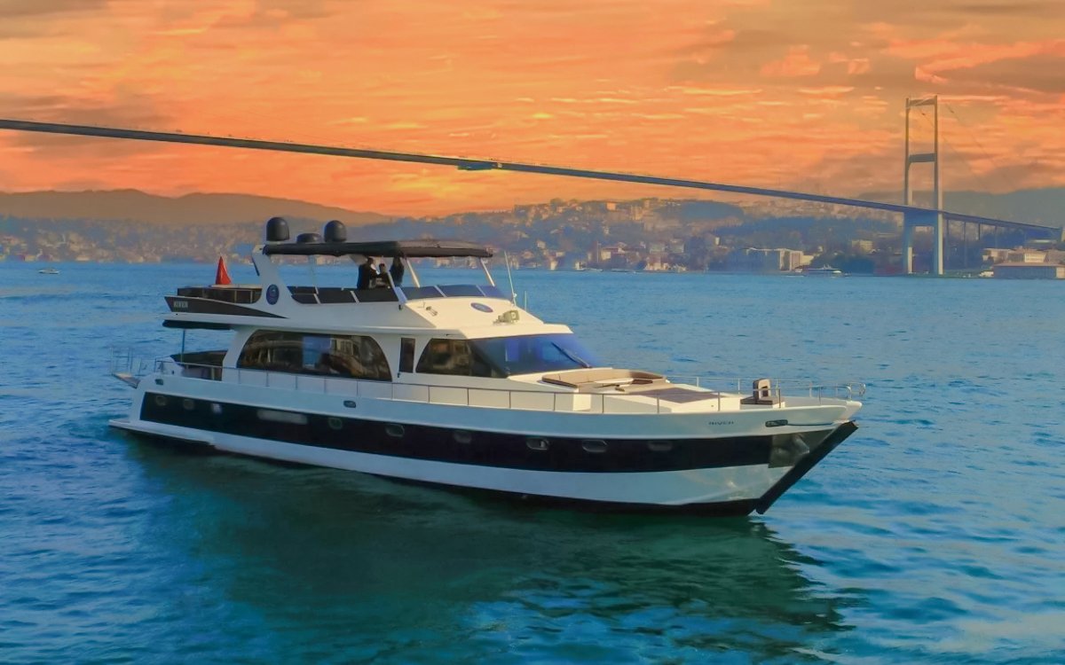 Luxury yacht cruising on the Bosphorus at sunset with a bridge in the background.