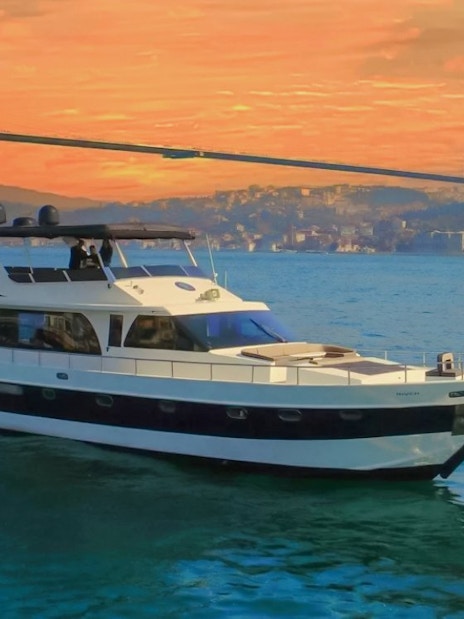 Luxury yacht cruising on the Bosphorus at sunset with a bridge in the background.