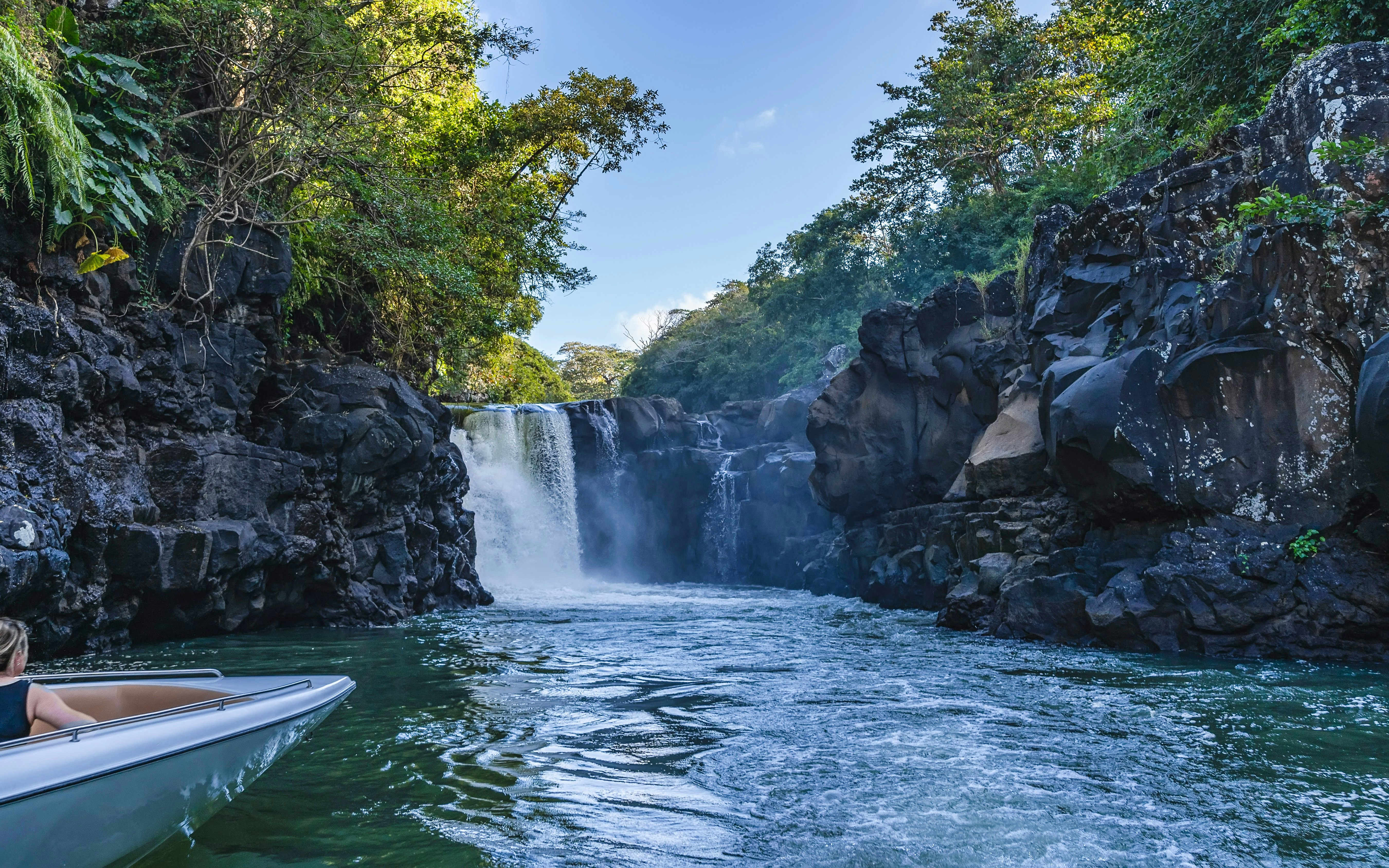 Boat approaching Grand River South East Waterfall surrounded by lush greenery and rocky cliffs.