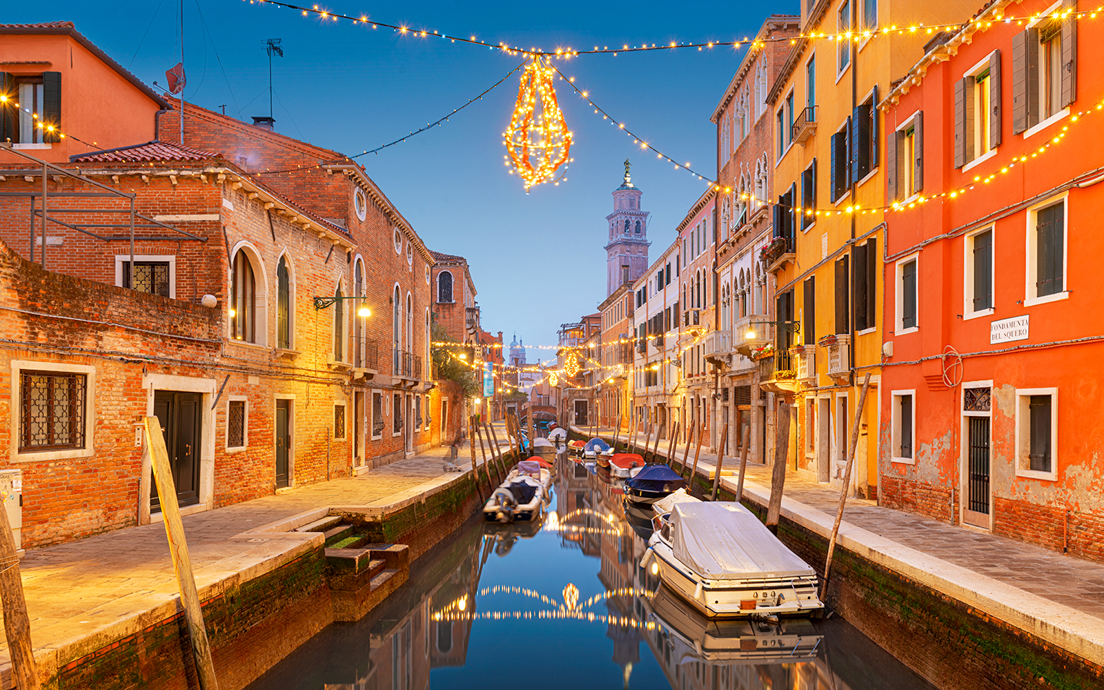 Venice canal with gondolas and Christmas lights reflecting on the water.