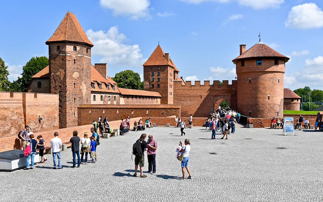 Visitors exploring the courtyard of Malbork Castle with audio guides.