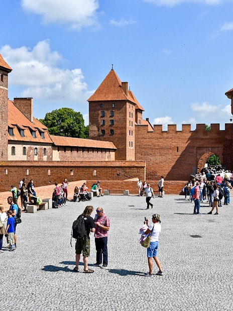 Visitors exploring the courtyard of Malbork Castle with audio guides.
