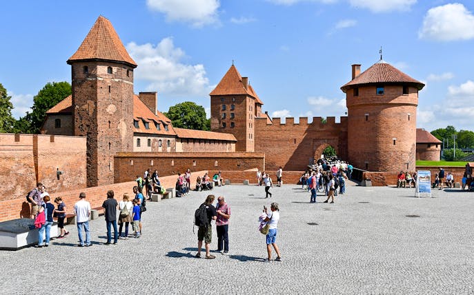 Visitors exploring the courtyard of Malbork Castle with audio guides.