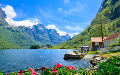 Nærøyfjord with snow-capped mountains, red-roofed house, and vibrant flowers in Norway.