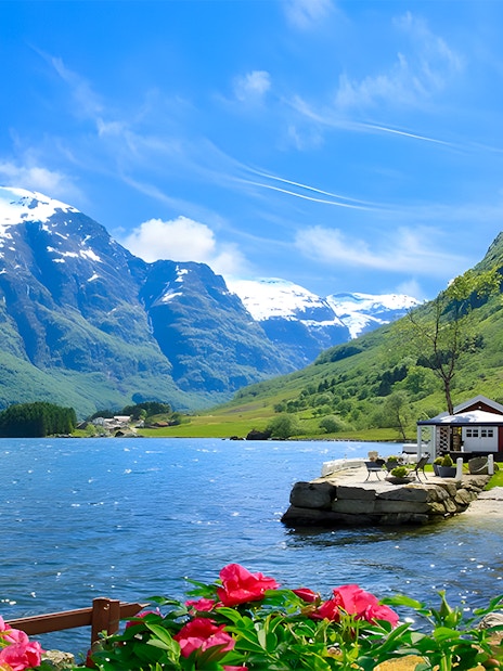 Nærøyfjord with snow-capped mountains, red-roofed house, and vibrant flowers in Norway.