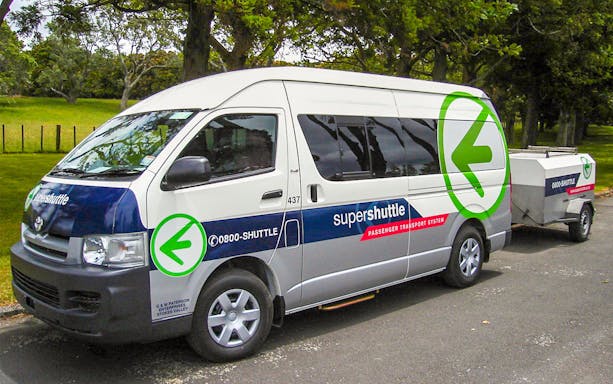 Super Shuttle van parked in a green area, used for airport transfers.