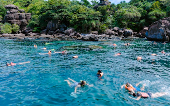 Snorkelers exploring clear waters near rocky coastline on 4 island day trip.