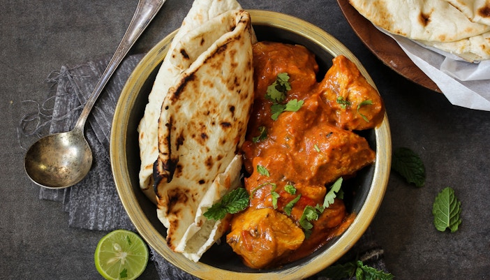 Naan and butter chicken garnished with cilantro in a bowl, with a spoon and lime wedge nearby.