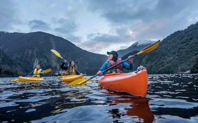 Kayakers paddling in Doubtful Sound fjord, view from Te Anau overnight cruise, New Zealand.