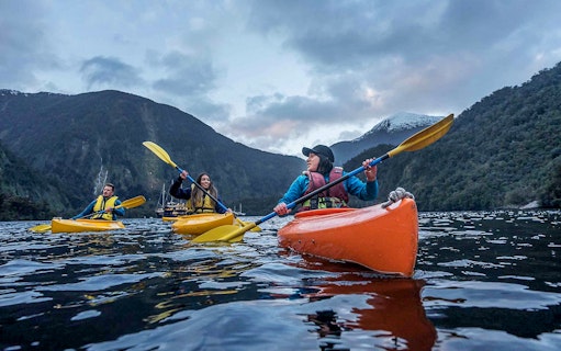 Kayakers paddling in Doubtful Sound fjord, view from Te Anau overnight cruise, New Zealand.