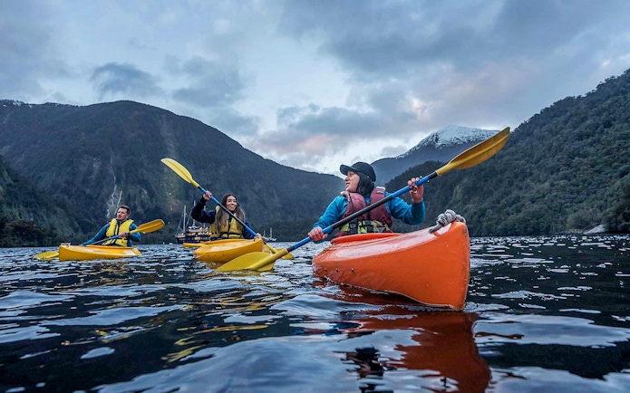 Kayakers paddling in Doubtful Sound fjord, view from Te Anau overnight cruise, New Zealand.
