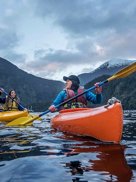 Kayakers paddling in Doubtful Sound fjord, view from Te Anau overnight cruise, New Zealand.