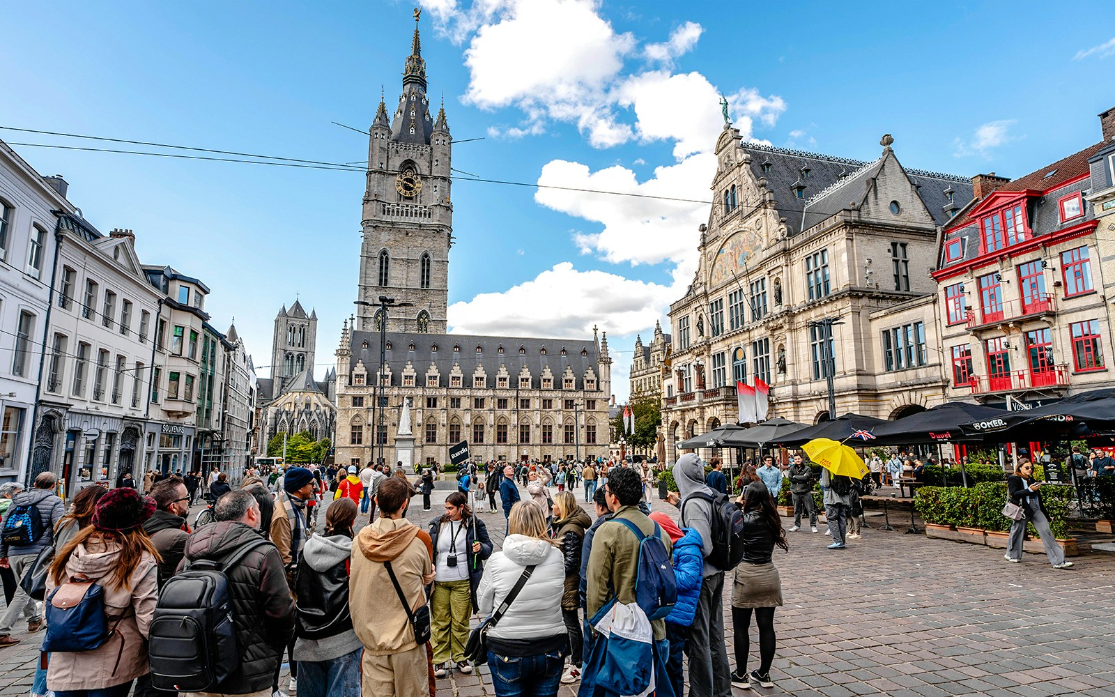 Tourists gather in Ghent's historic center with the Belfry of Ghent in the background.