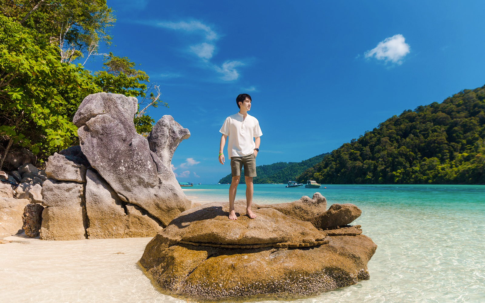 Tourist standing on rock at Chong Khad Bay with clear water and lush hills.