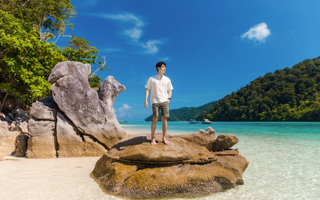 Tourist standing on rock at Chong Khad Bay with clear water and lush hills.