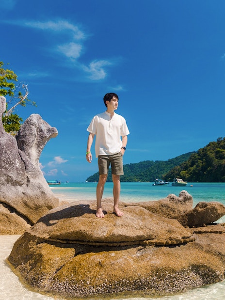 Tourist standing on rock at Chong Khad Bay with clear water and lush hills.