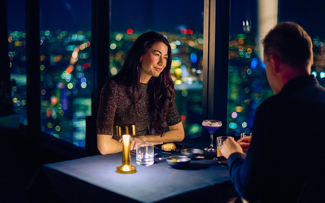 Couple dining at Altitude experience, Melbourne Skydeck with city lights in background.